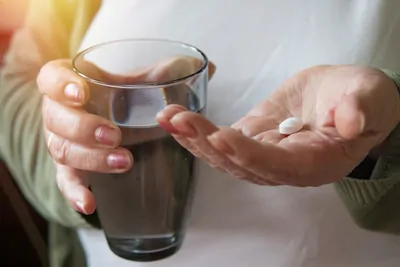 Woman holding a glass of water in one hand and pill in the other